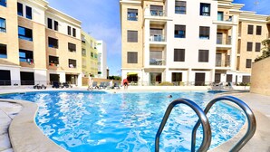 Una piscina con escalera metálica, rodeada de edificios de varios pisos con balcones y mobiliario exterior.