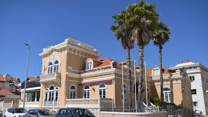 Un hotel de estilo arquitectónico clásico, con un balcón y una palmera en primer plano.