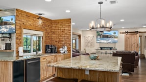 A modern kitchen with a brick accent wall, granite countertops, and a large island with bar stools.