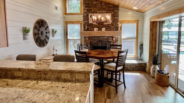 A modern kitchen with a stone fireplace, wooden ceiling, and a large island with seating.