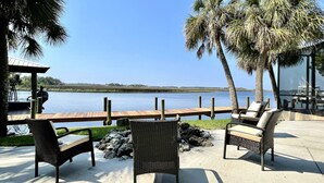 An outdoor patio with wicker furniture, a wooden deck, and a view of a calm body of water.