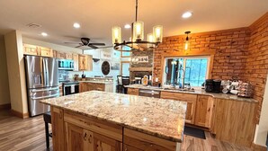 A kitchen with wooden cabinets, a granite countertop, stainless steel appliances, and a brick accent wall.