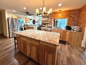 A kitchen with wooden cabinets, a granite countertop, stainless steel appliances, and a brick accent wall.