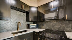 Une cuisine moderne avec des meubles de rangement noirs, un four à micro-ondes, une cuisinière et un évier.