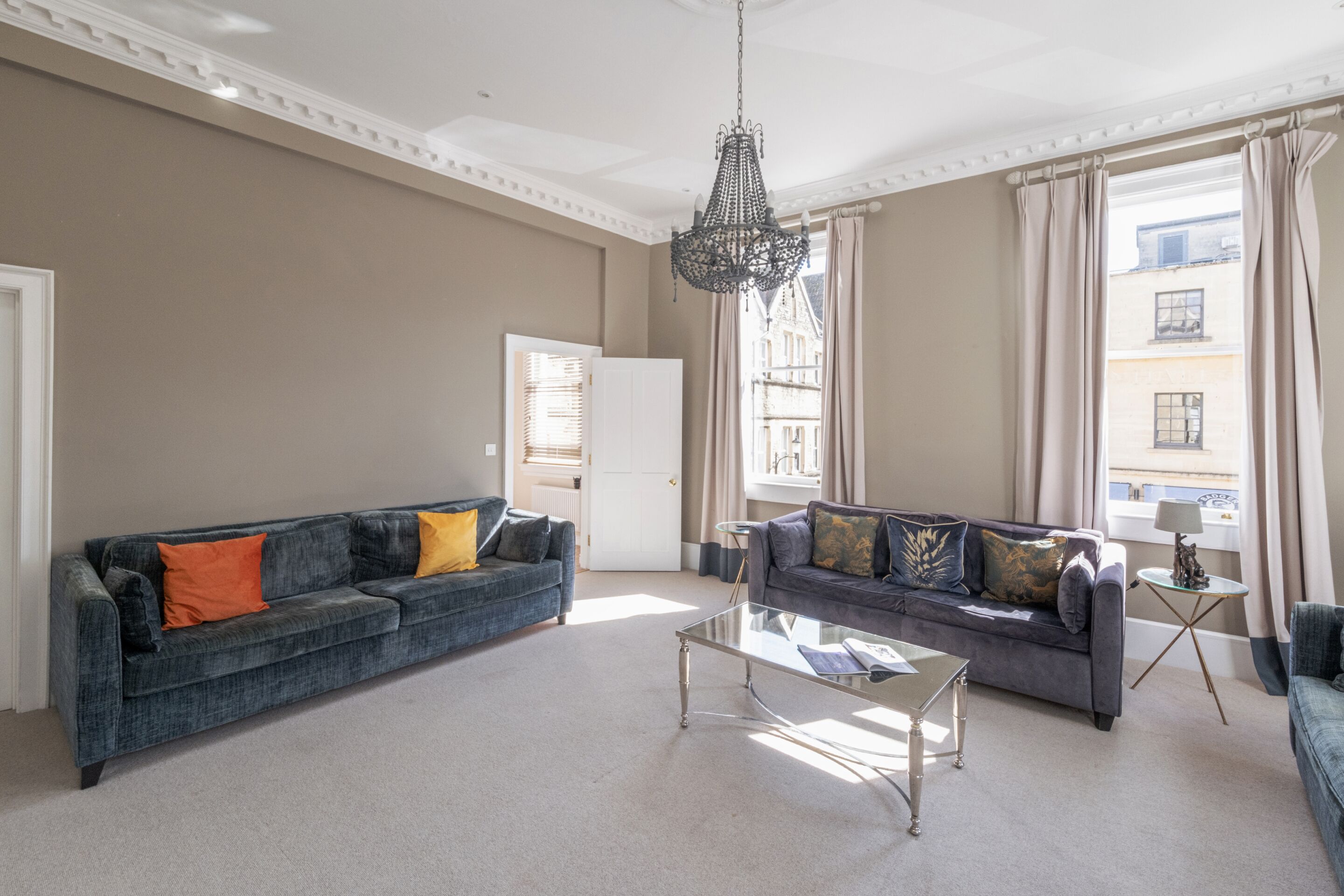 A spacious living room with two sofas, a glass coffee table, and a chandelier.