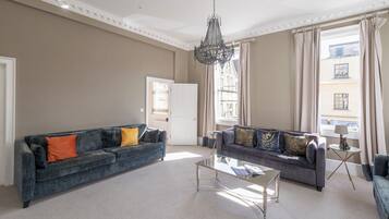 A spacious living room with two sofas, a glass coffee table, and a chandelier.