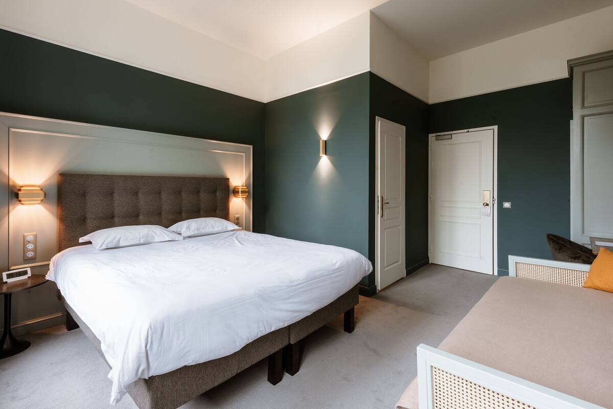 Een slaapkamer met een groot bed, nachtlampjes, een kledingkast en een klein tafeltje.