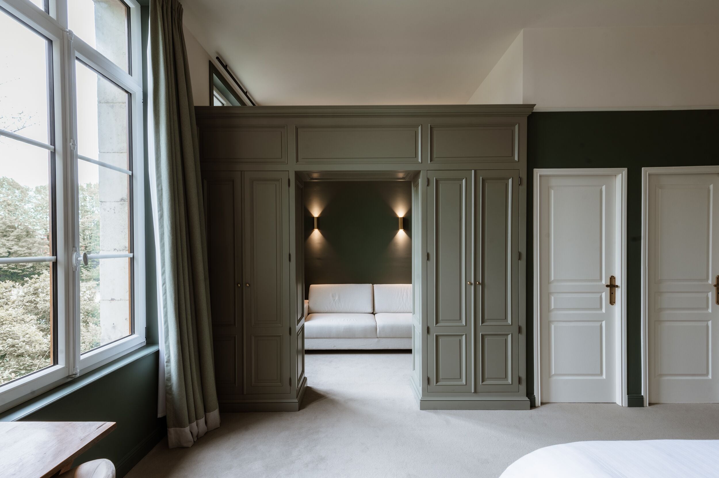 A bedroom with a large window, a sofa, and built-in wardrobes.