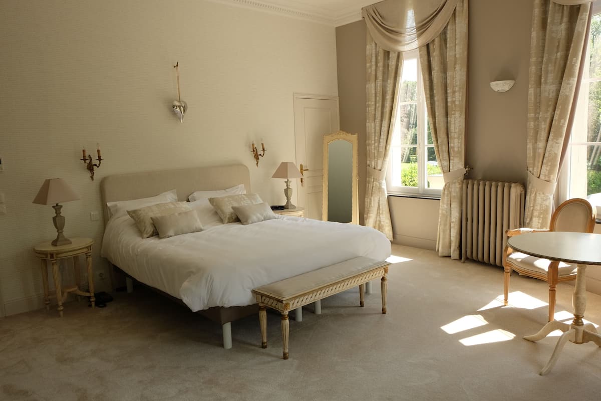 Een slaapkamer met een groot bed, nachtkastjes, een spiegel, een stoel en een raam met gordijnen.