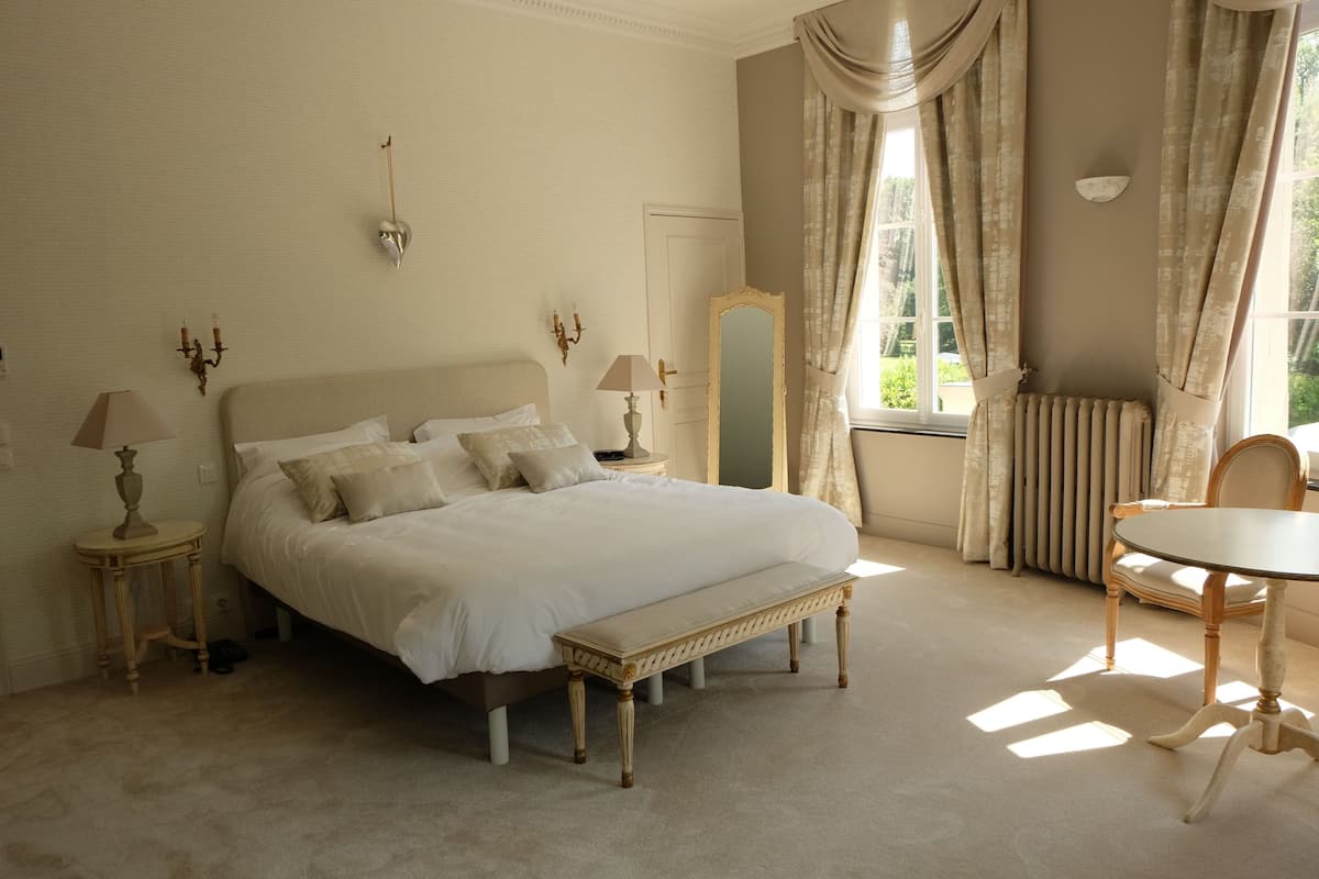 Een slaapkamer met een groot bed, nachtkastjes, een spiegel, een ronde tafel en een bank.