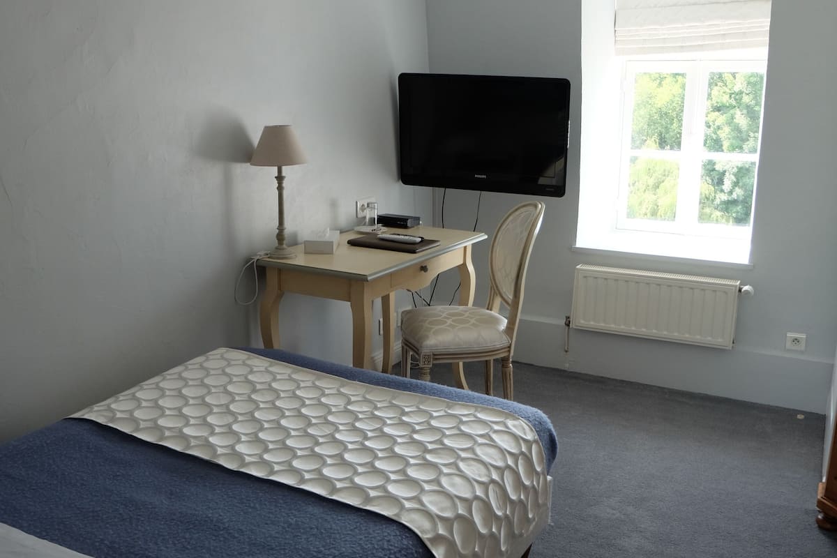 Een slaapkamer met een bed, een bureau, een stoel, een televisie en een raam.