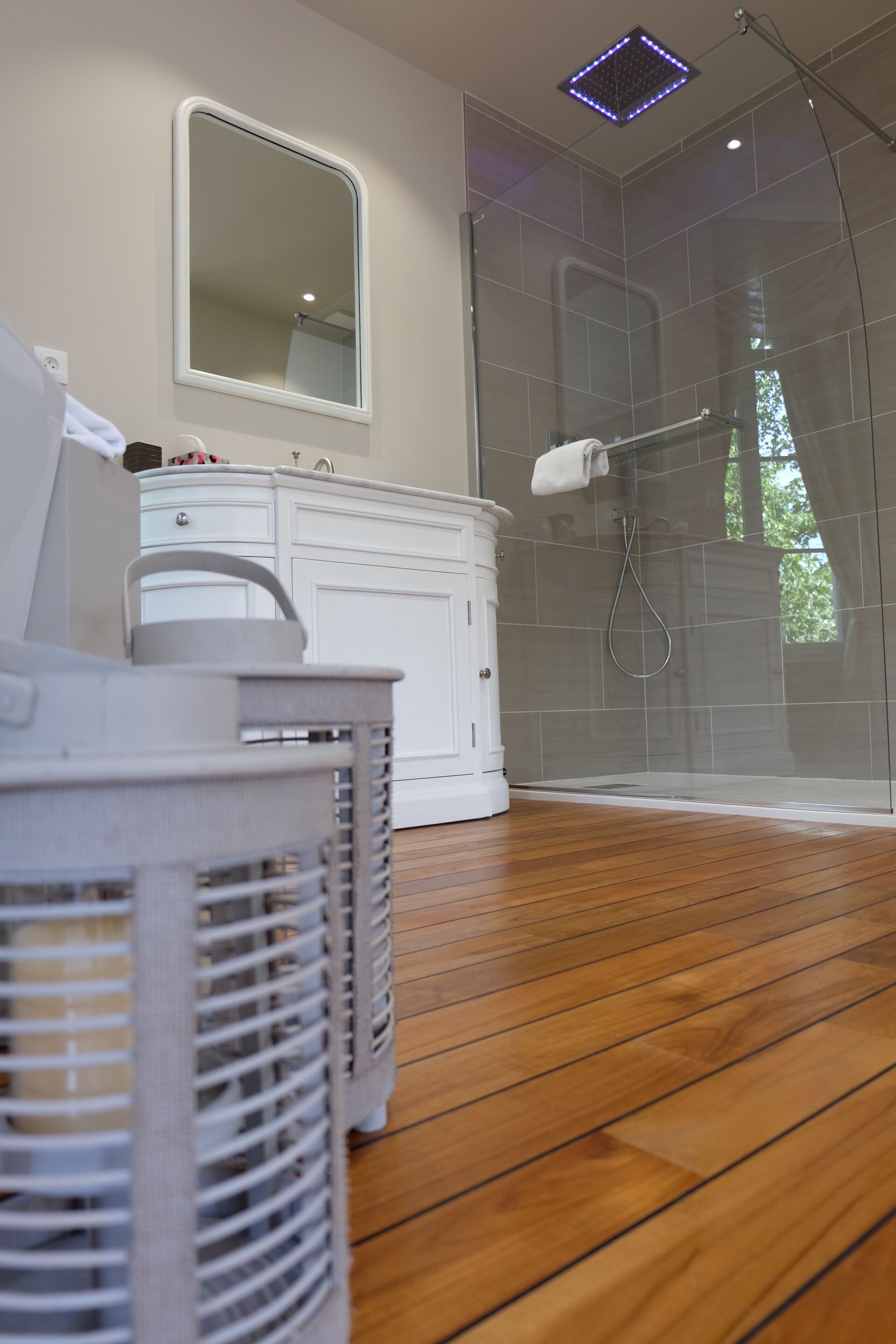 Un baño moderno con cabina de ducha de vidrio, tocador blanco y suelo de madera.