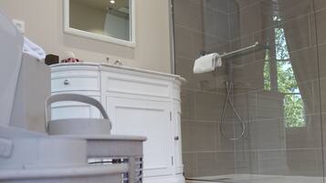 Un baño moderno con cabina de ducha de vidrio, tocador blanco y suelo de madera.