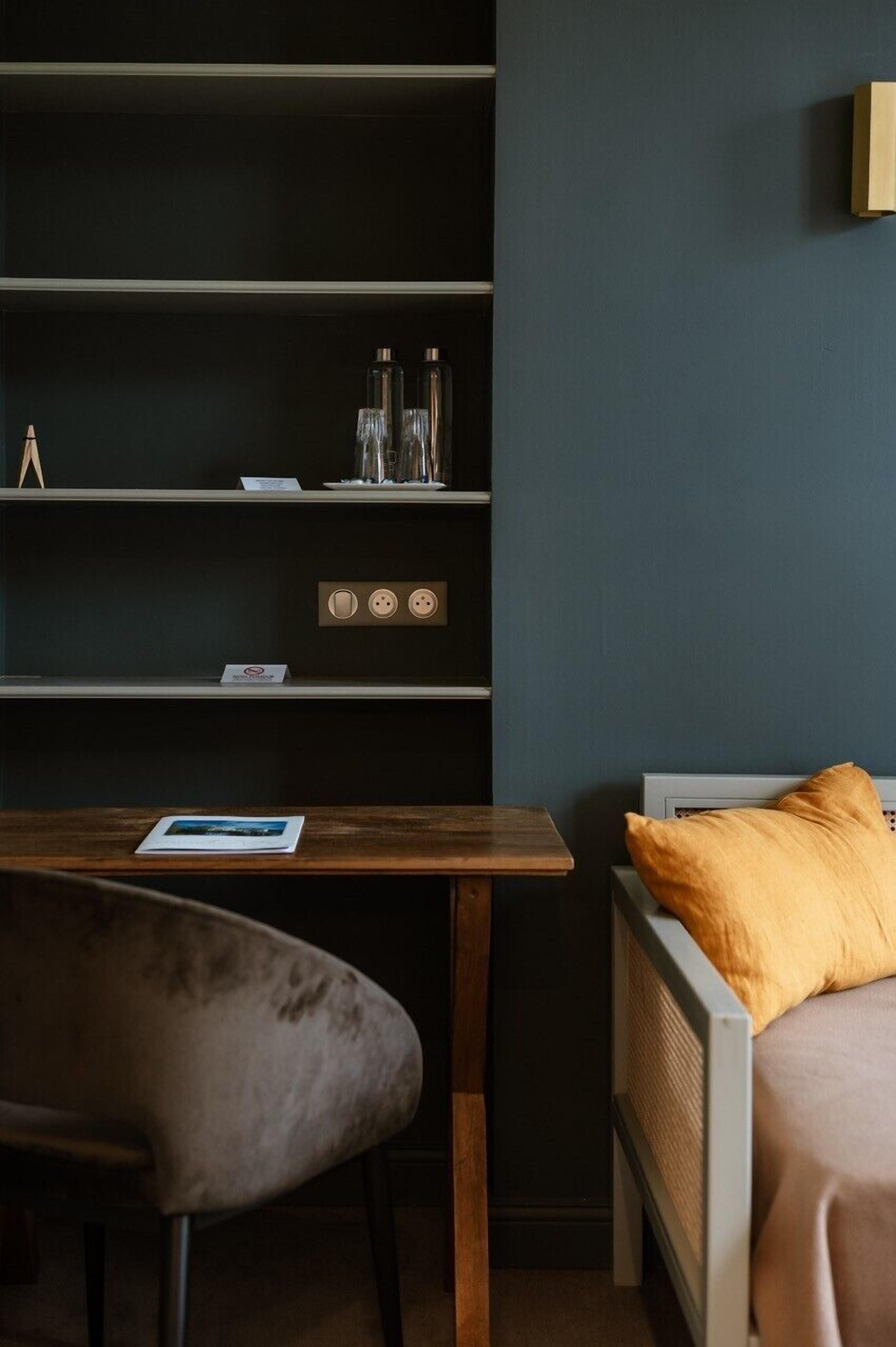 A room with a bed, a desk, and a chair. There are shelves with items on them.