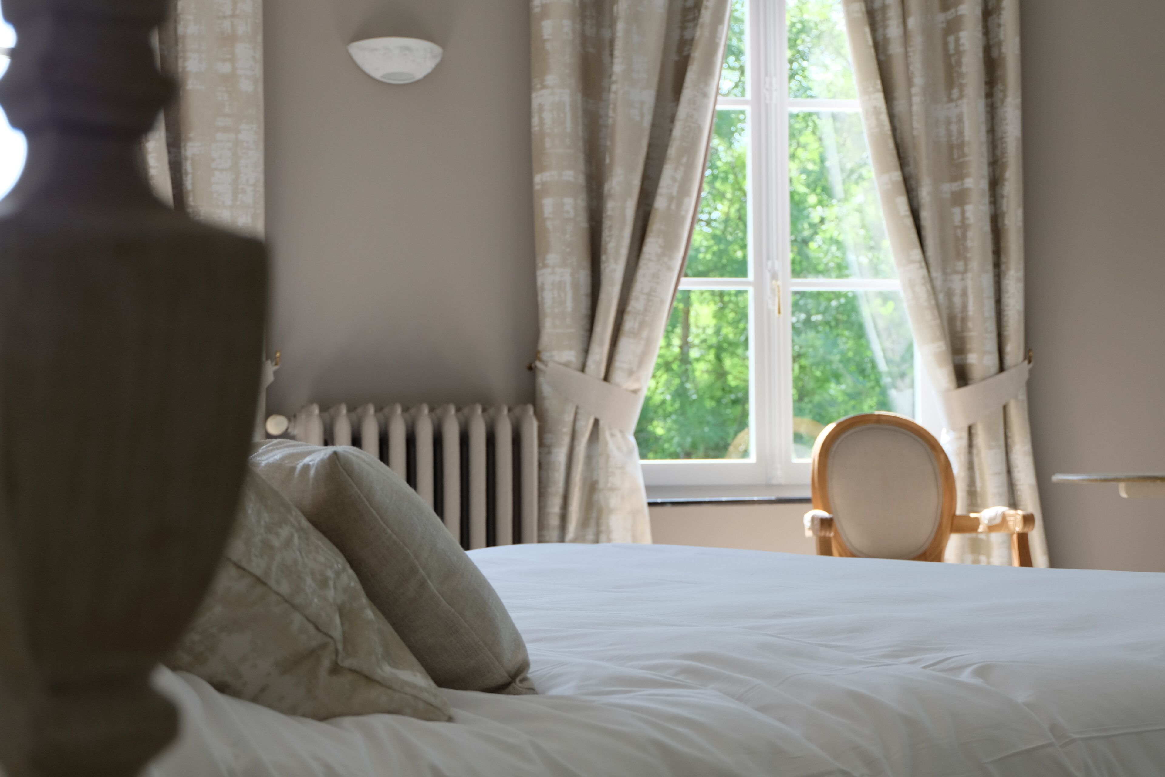 A bedroom with a large bed, a chair, a radiator, and a window with curtains.
