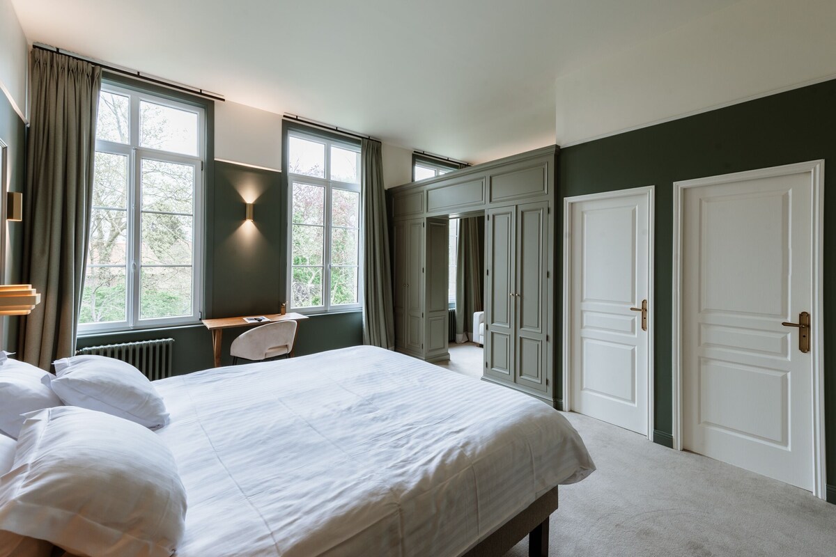 A hotel room with a large bed, a desk, and two doors.