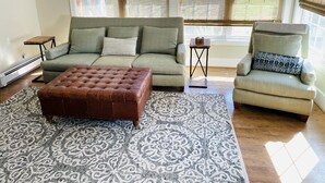 A living room with a sofa, armchair, ottoman, patterned rug, and a small table.