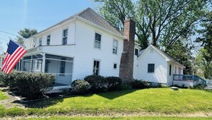 A two-story white house with a brick chimney, a front porch, and an American flag.