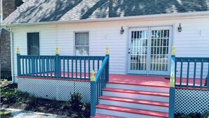 A white house with a red and blue porch, a set of stairs leading to a door with a window, and a small garden area.