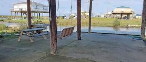 A covered outdoor area with a concrete floor, wooden benches, and a swing.