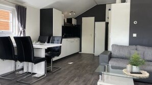 Una sala de estar moderna con un sofá gris, una mesa de centro de vidrio y un comedor con una mesa blanca y sillas negras.