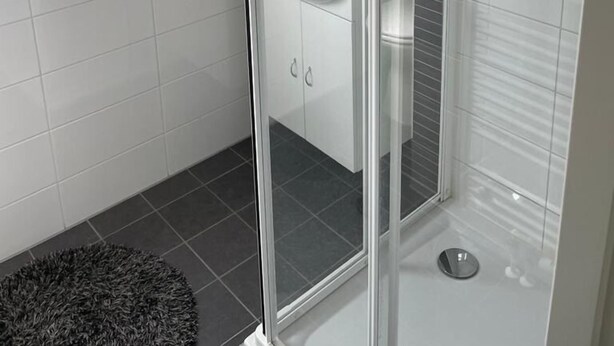 A modern bathroom with a glass shower enclosure, white tiles, and a visible sink. - Familien Wood Lodge am Geiseltalsee (Mücheln (Geiseltal))