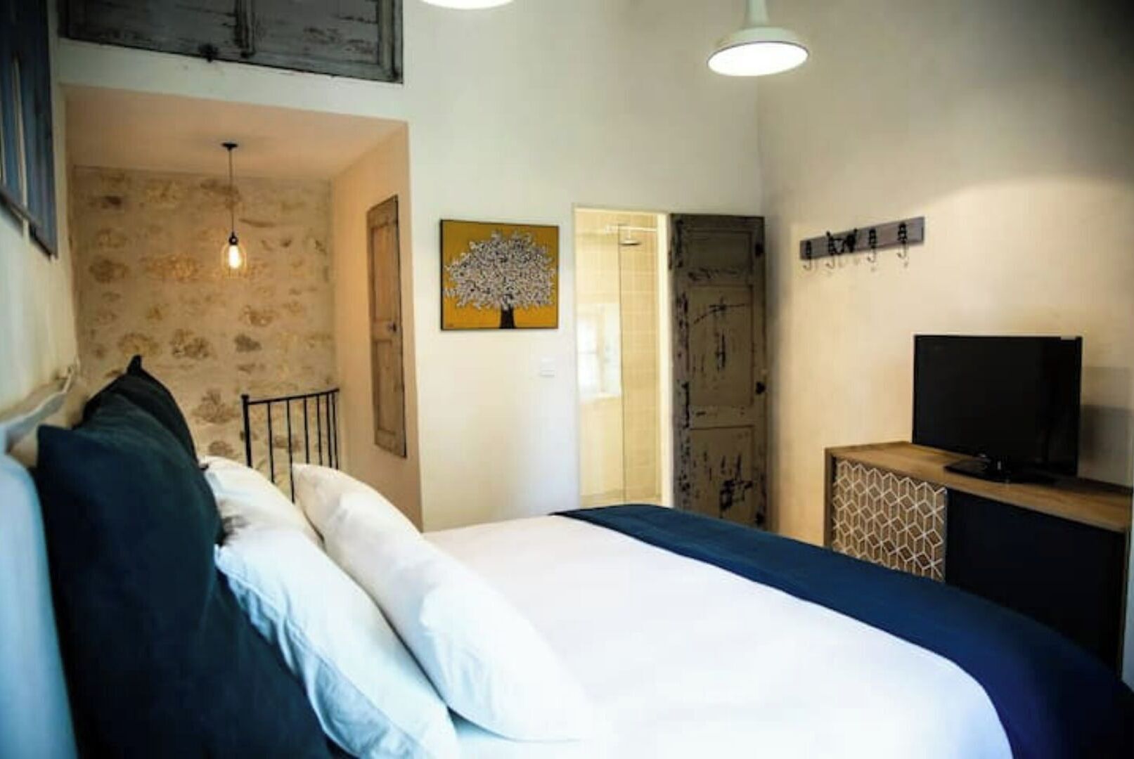 A bedroom with a bed, a TV, a painting, and a door leading to another room.