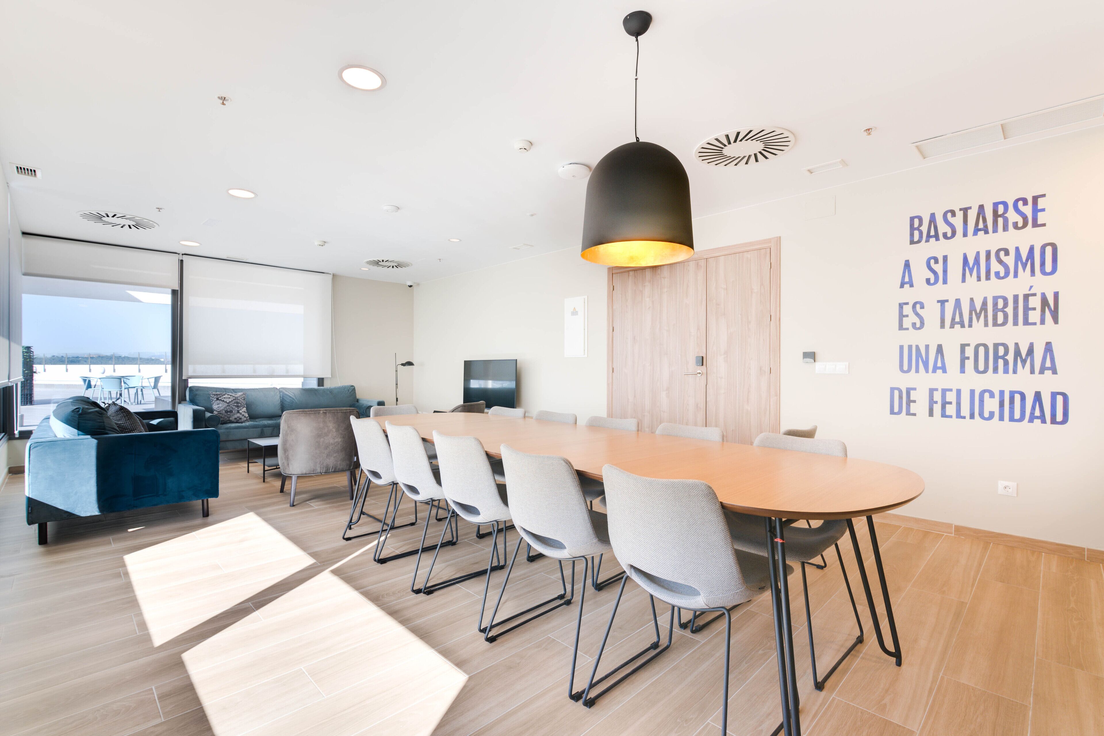 Uma sala de reunião moderna com uma mesa comprida, cadeiras e uma luminária pendente grande.