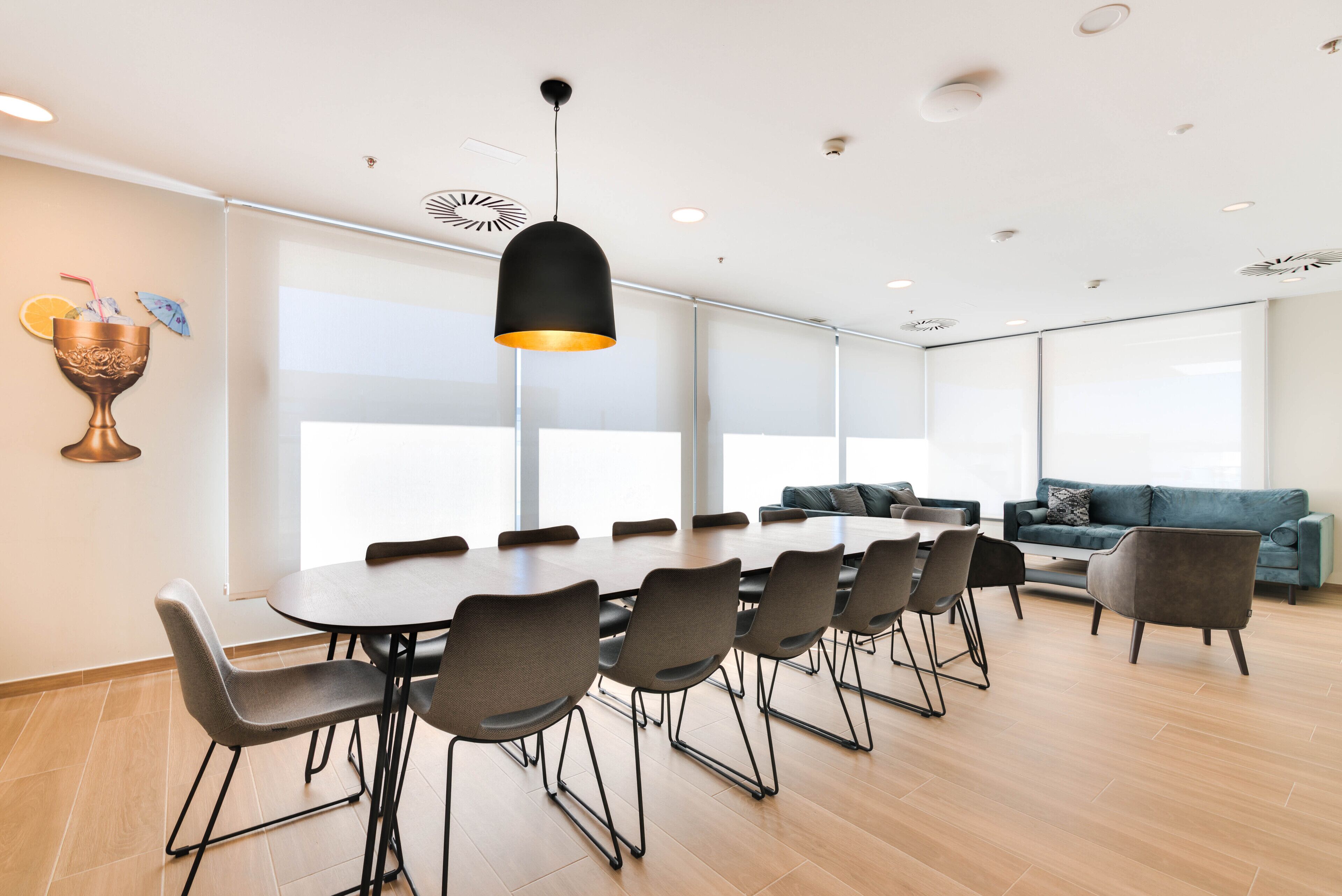A modern meeting room with a large table, chairs, and a hanging light fixture.