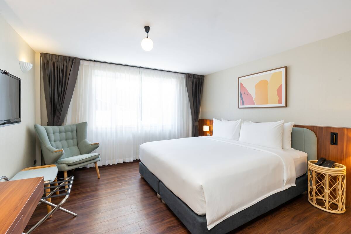 A hotel room with a large bed, a chair, a desk, and a television.