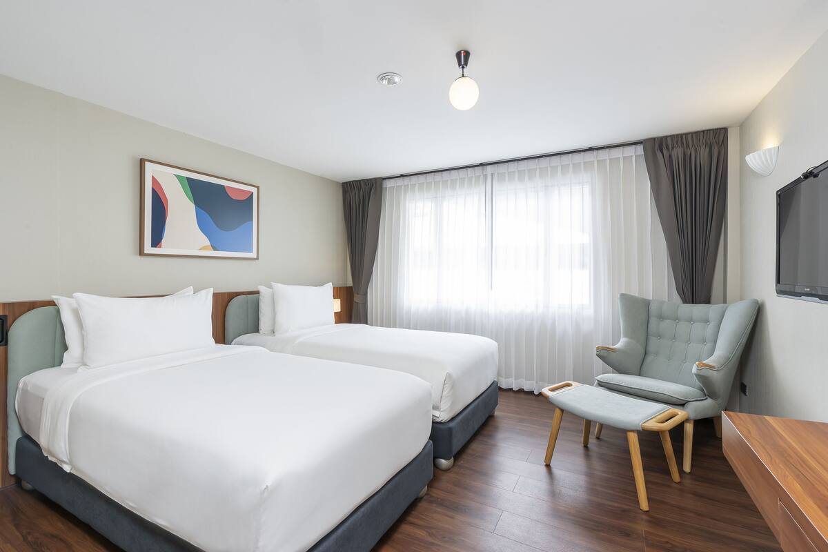 A hotel room with two beds, a chair, a desk, and a painting on the wall.