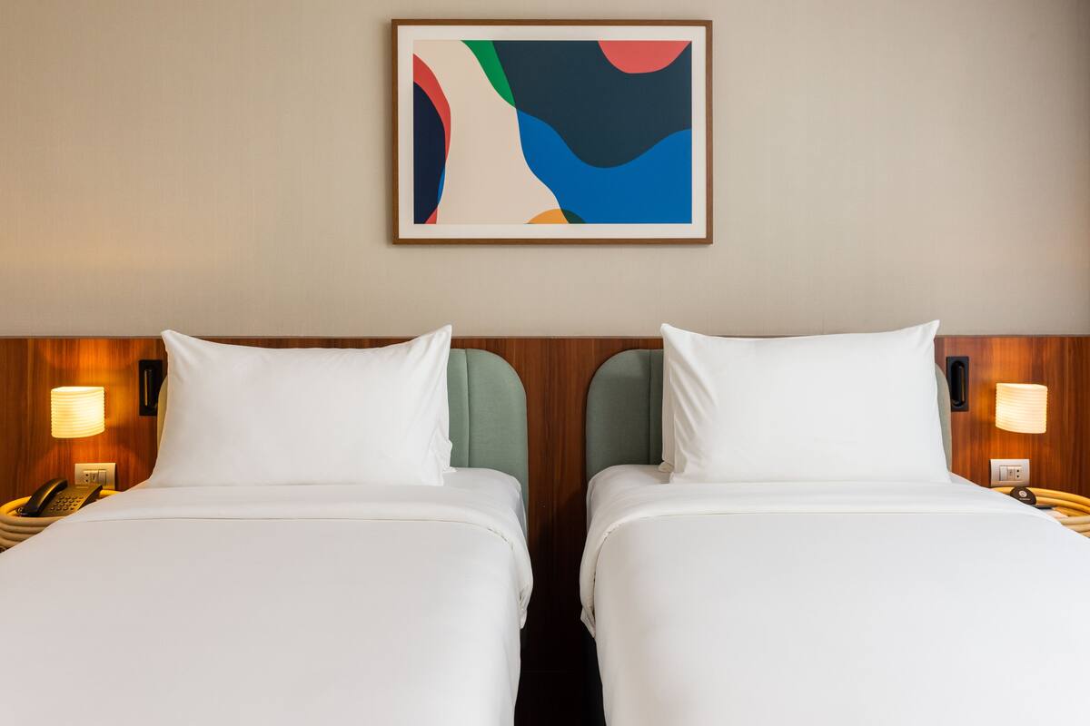 A hotel room with two beds, each with white bedding and a wooden headboard. There are bedside lamps and a telephone on each nightstand.