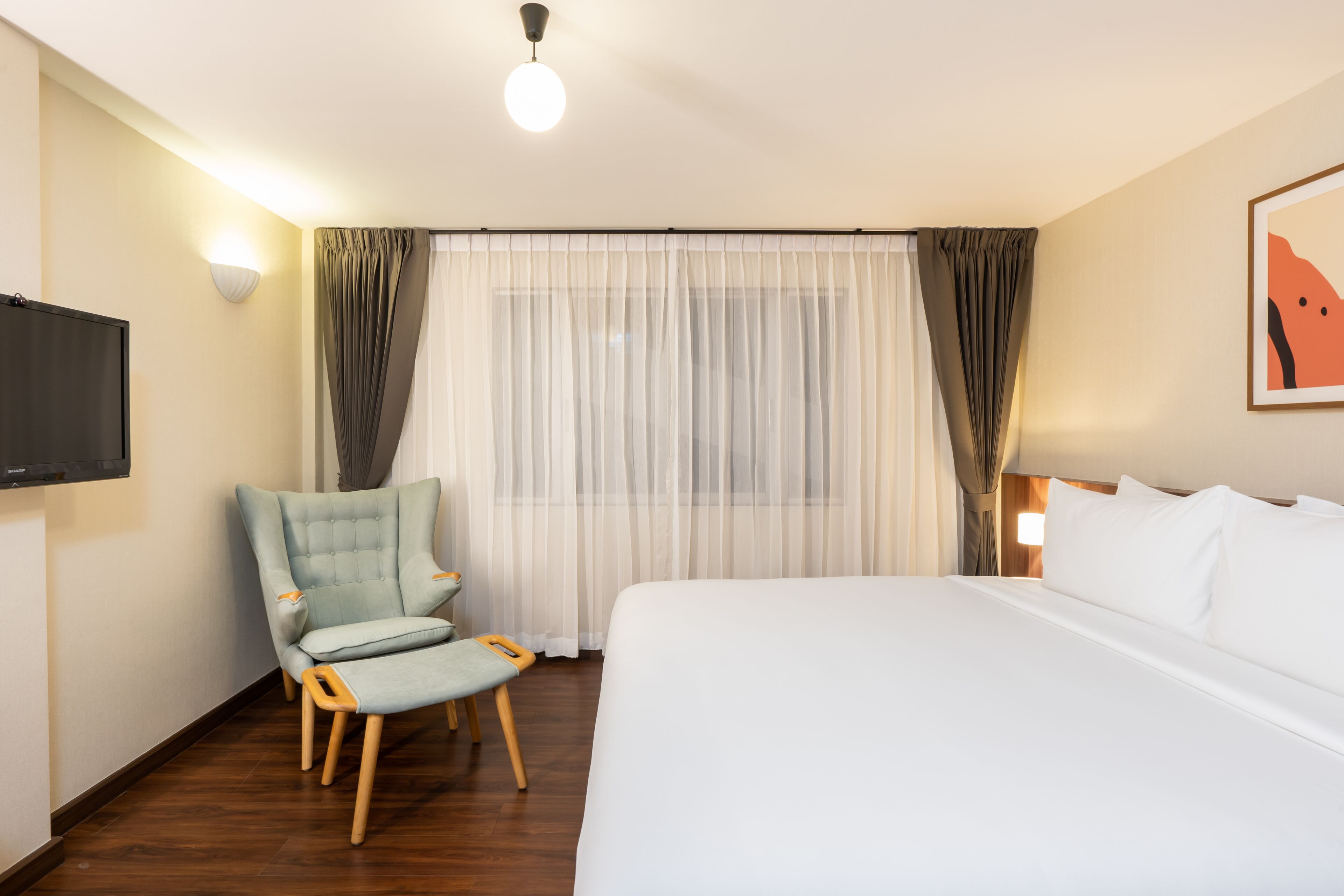 Een hotelkamer met een groot bed, een stoel, een televisie en een raam met dunne gordijnen.