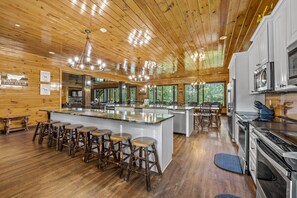 A spacious kitchen with wooden ceilings, a large island with stools, and modern appliances. - Luxury lodge with 13 king suites, theater, game room & views! (Gatlinburg)