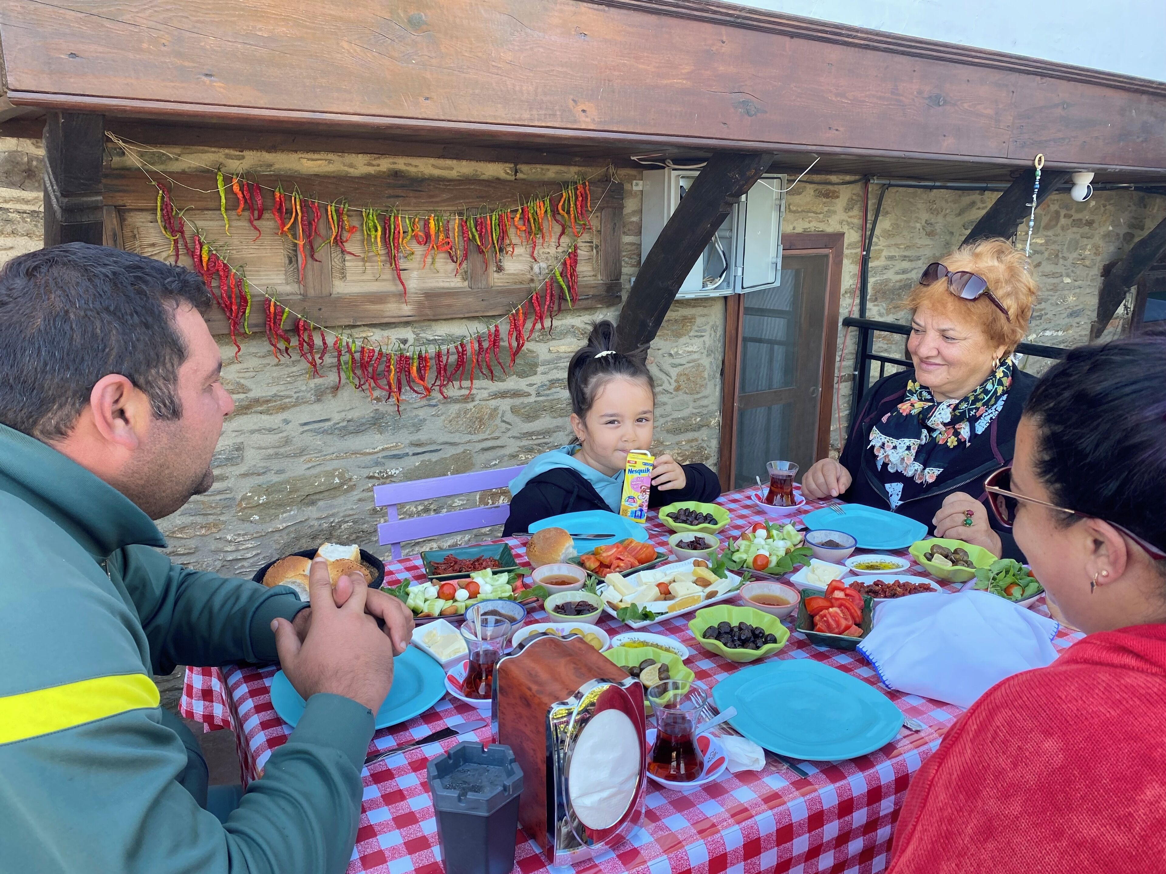 Una familia comiendo al aire libre en una mesa con diversos platos, como ensaladas, pan y una jarra de té.