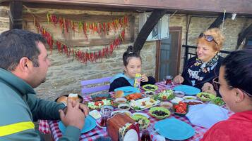 Una familia comiendo al aire libre en una mesa con diversos platos, como ensaladas, pan y una jarra de té.