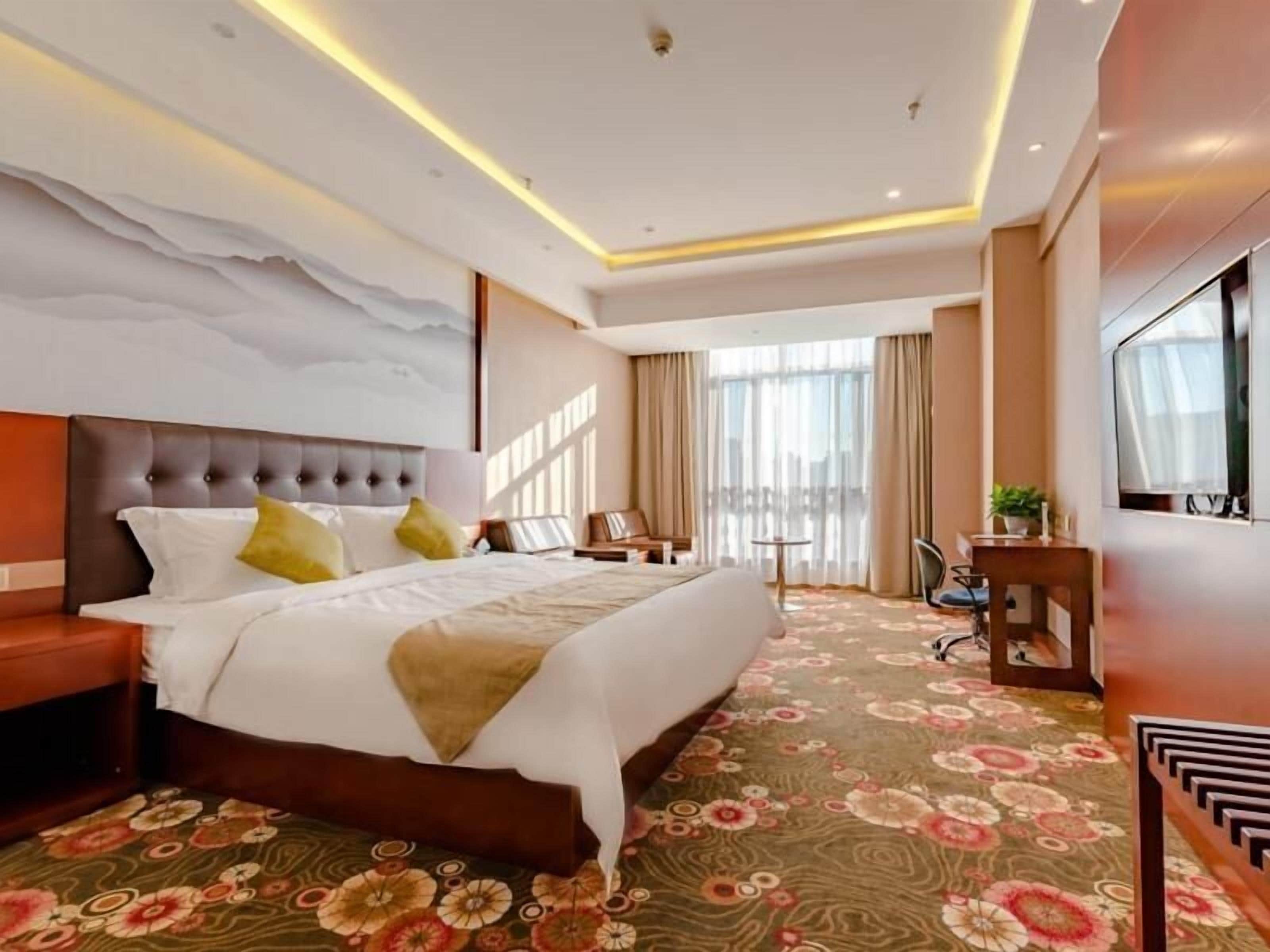 Ein modernes Hotelzimmer mit einem großen Bett, einem Flachbildfernseher, einem Schreibtisch und Balkonblick.