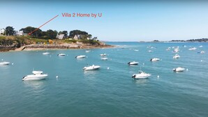 Eine Küstenlandschaft mit mehreren Booten auf dem Wasser und einer Villa am Ufer, die mit „Villa 2 Home by U“ beschriftet ist.