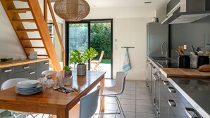 Eine moderne Küche mit einem Holztisch, weißen Stühlen und einem großen Fenster mit Blick auf Grünflächen.