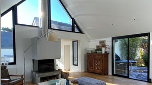 Ein modernes Wohnzimmer mit Kamin, Holzböden und großen Fenstern mit Blick ins Freie.