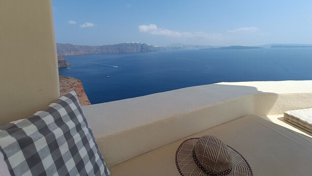 A balcony with a view of the sea, a checkered pillow, and a woven chair. - Elias Cave Oia 270o Caldera View  Bioclimatic Eco House Santorini  (Οία)