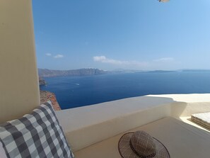A balcony with a view of the sea, a checkered pillow, and a woven chair. - Elias Cave Oia 270o Caldera View  Bioclimatic Eco House Santorini  (Οία)