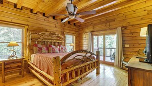 Un dormitorio de cabaña de madera con una cama grande, un ventilador de techo y vistas al exterior.