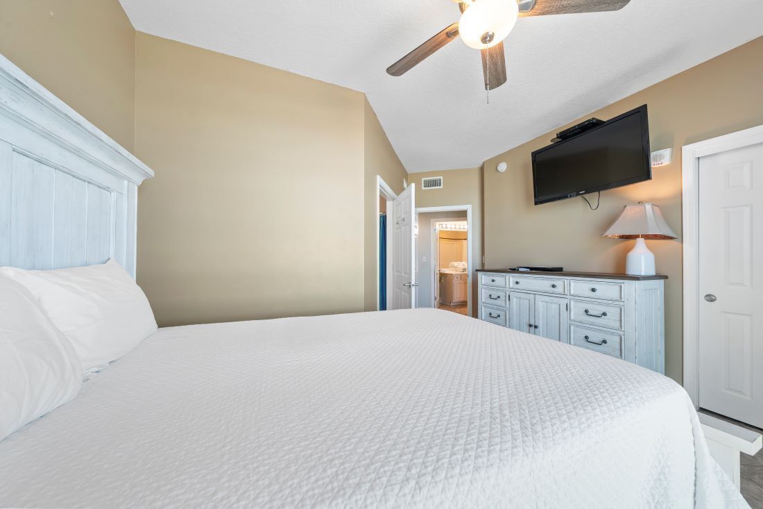 A bedroom with a large bed, a ceiling fan, a television, and a dresser.