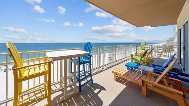 A balcony with a view of the beach and ocean, featuring wooden furniture and chairs. - Crystal Shores West 108- The Tide is Calling your Name! Can you Hear it? Book To (Gulf Shores)