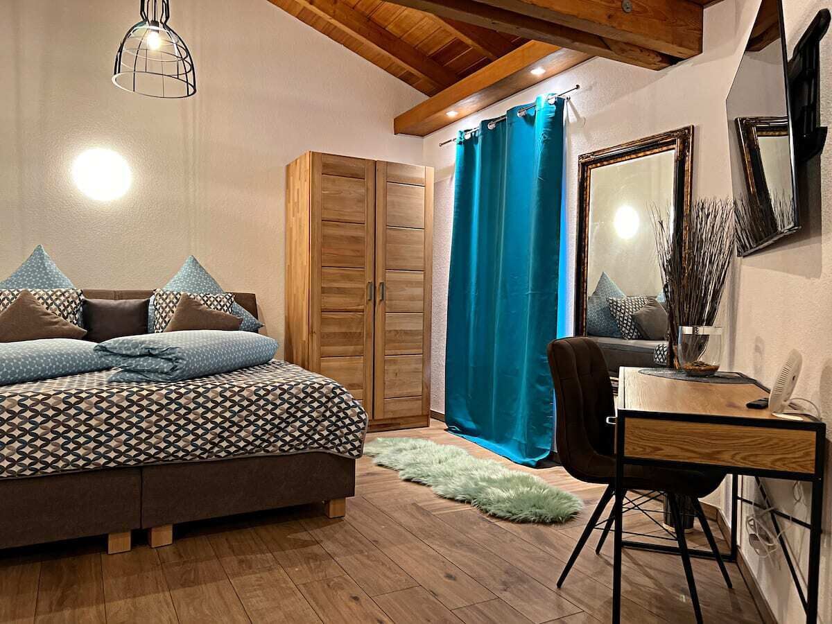 A bedroom with a bed, a desk, a chair, a wardrobe, and a mirror.