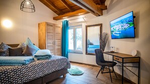 A bedroom with a bed, a desk, a chair, a TV, and a window with curtains. - Familien am Hang (Friedrichshafen)