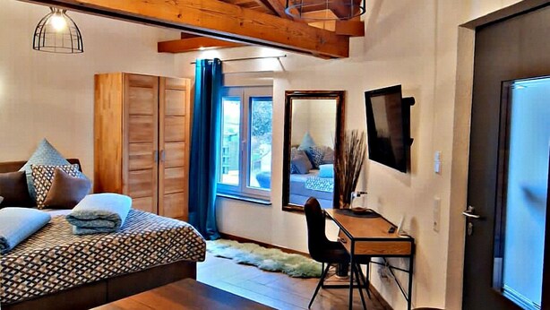 A cozy room with a wooden ceiling, a bed, a dining table, and a TV. - Familien am Hang (Friedrichshafen)