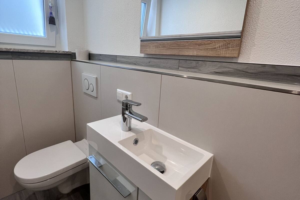 Ein modernes Badezimmer mit einer weißen Toilette, einem Waschbecken mit Spiegel darüber und einem Fenster mit Jalousien.