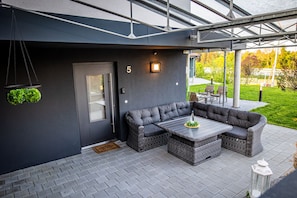 A modern outdoor seating area with a dark-colored sofa and a table, a door with a glass panel, and a number '5' on the wall.